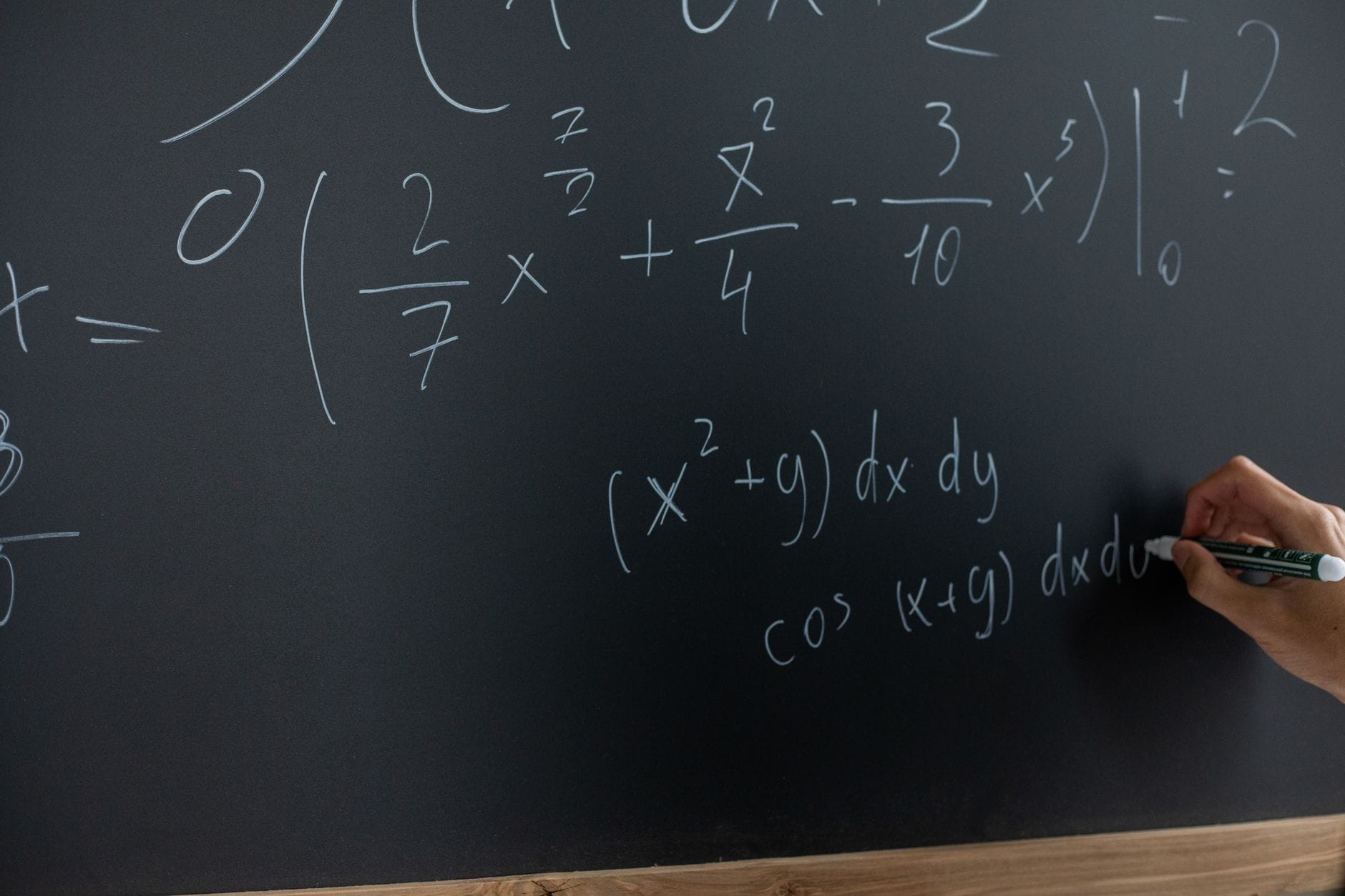 Ręka nauczyciela zapisuje wzory matematyczne na tablicy w klasie